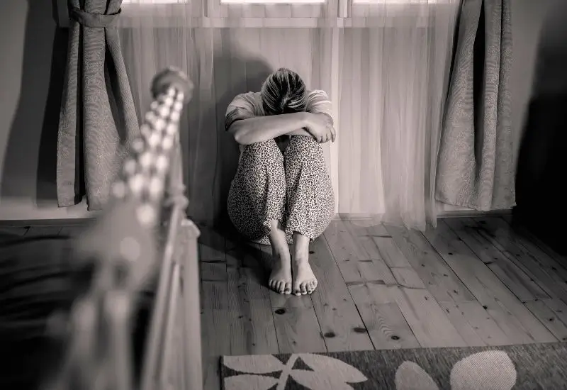 Unhappy woman sitting on the floor with her head facing down in the bedroom